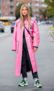 Blonde model in a pink trench coat with white sneakers with black and green stripes