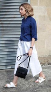 Blonde woman wearing blue button-down shirt, white skirt and white summer sandals walking