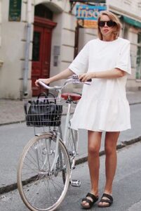 Blonde woman in white dress with black sandals pushing bicycle