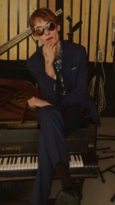 White woman in sunglasses and pantsuit sitting on piano
