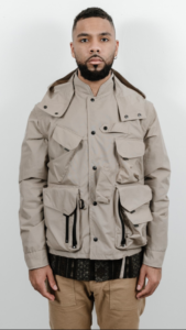Black male model styled in large beige jacket with multiple pockets